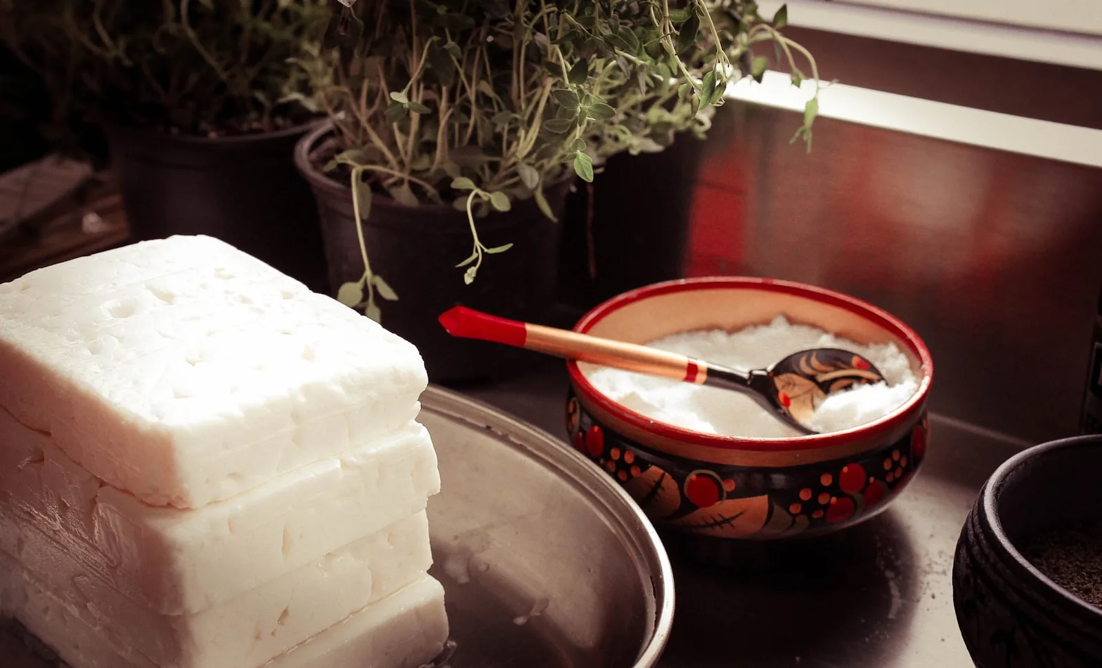 A white plate of fresh fromage blanc topped with finely chopped chives and garlic, with cherry tomatoes and a slice of bread on the side