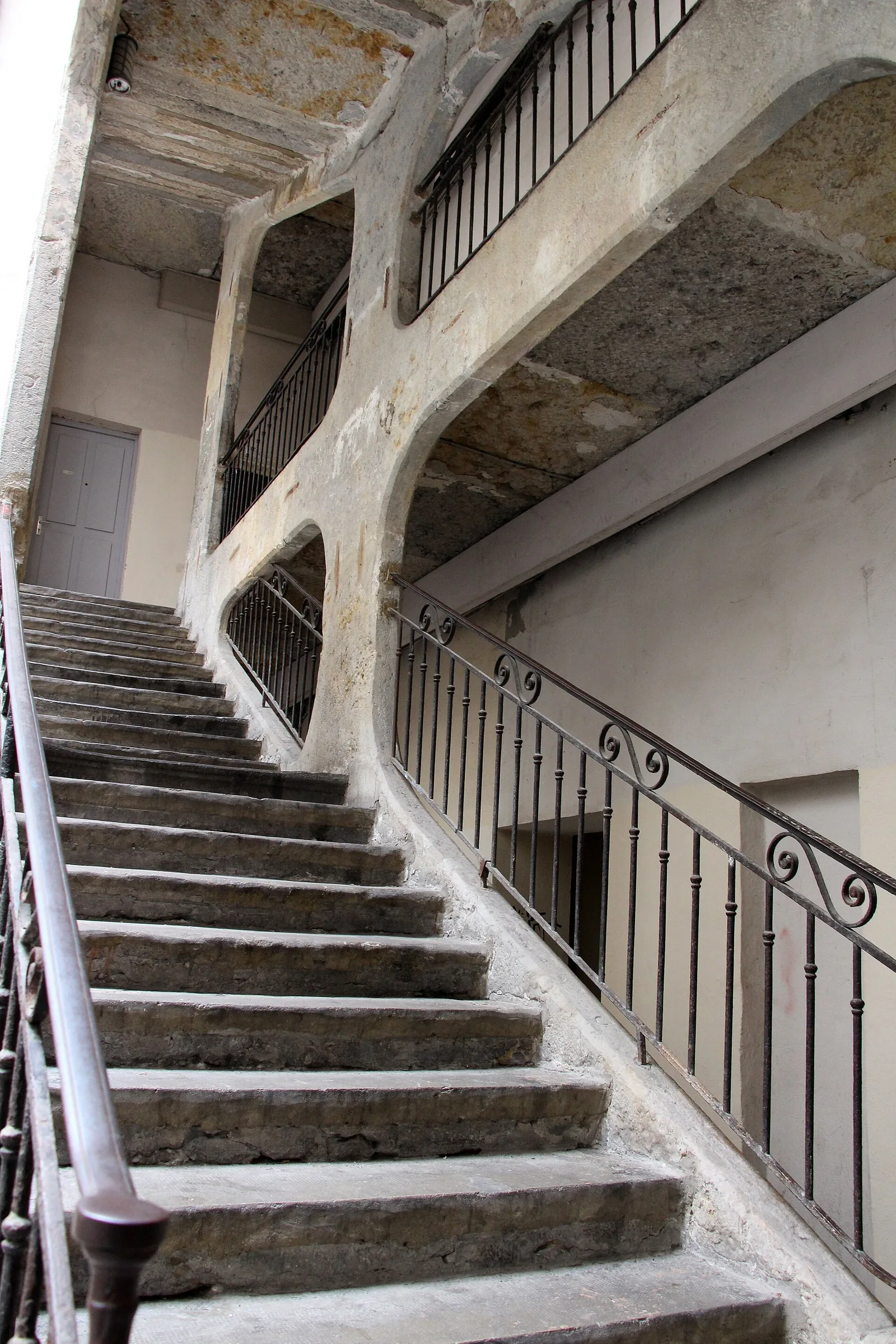 A Renaissance stone staircase in a traboule passage climbing through an arched doorway, courtyard light falling from above