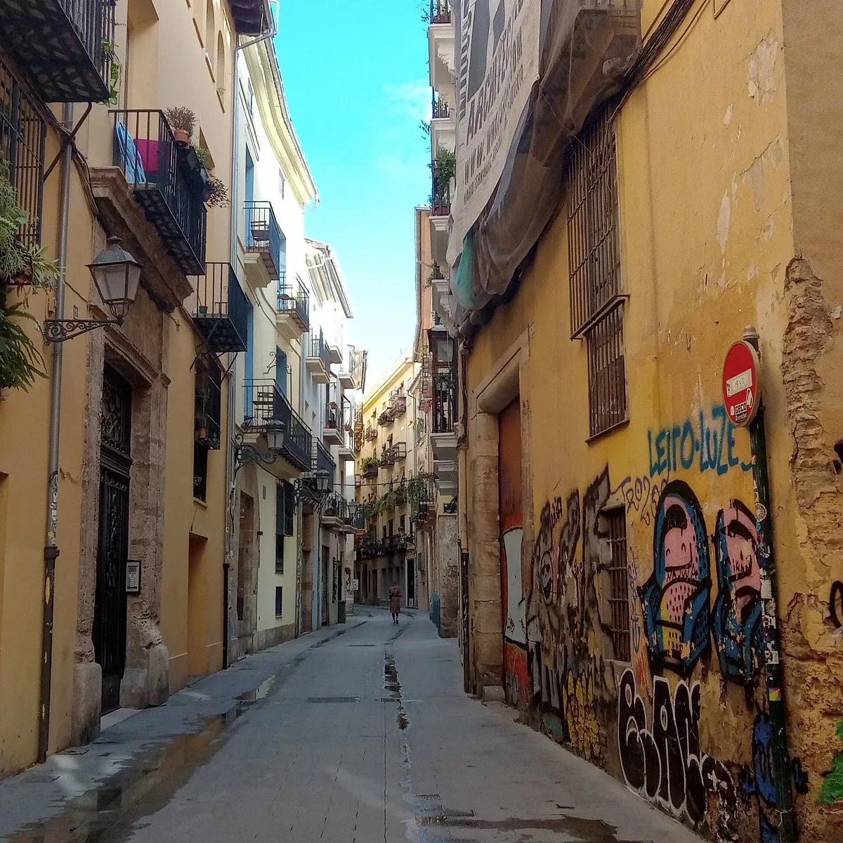 A narrow old-town alley with yellow lime walls, cast-iron balconies and a single street lamp