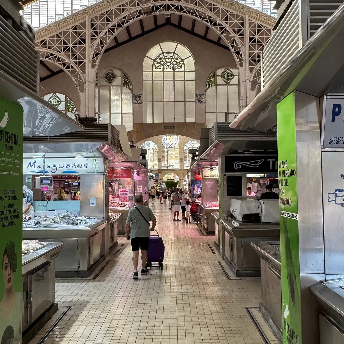 A covered market hall with arched windows and tiled floor, stalls on either side