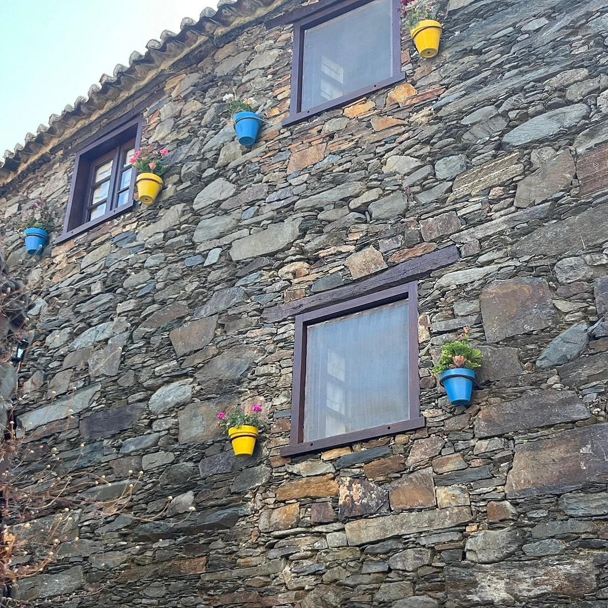 Close-up of a schist-stone quinta facade, with two windows and small blue and yellow flower pots fixed into the wall.